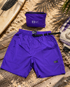 Bañador Salty Crew Raid Packable Short Purple Heart morado sobre escenario lifestyle de playa con tabla de surf y accesorios surferos para hombre