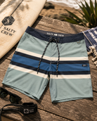 Bañador Salty Crew Stripe Boardshort Marine para hombre sobre fondo lifestyle surf con tabla de surf y accesorios premium de playa