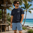 Bermudas Salty Crew Transom Tech Short Pilot Blue frente a palmeras del mar Caribe, fotografía editorial propia de THE SURF TOWN con modelo masculino surf lifestyle, tejido técnico ligero y estilo costero premium para verano