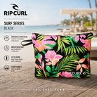 Bolsa Rip Curl Surf Series Black en fotografía editorial propia de THE SURF TOWN en beach club tropical premium con estampado floral, cierre de cremallera y diseño práctico para playa, viajes y accesorios de surf.