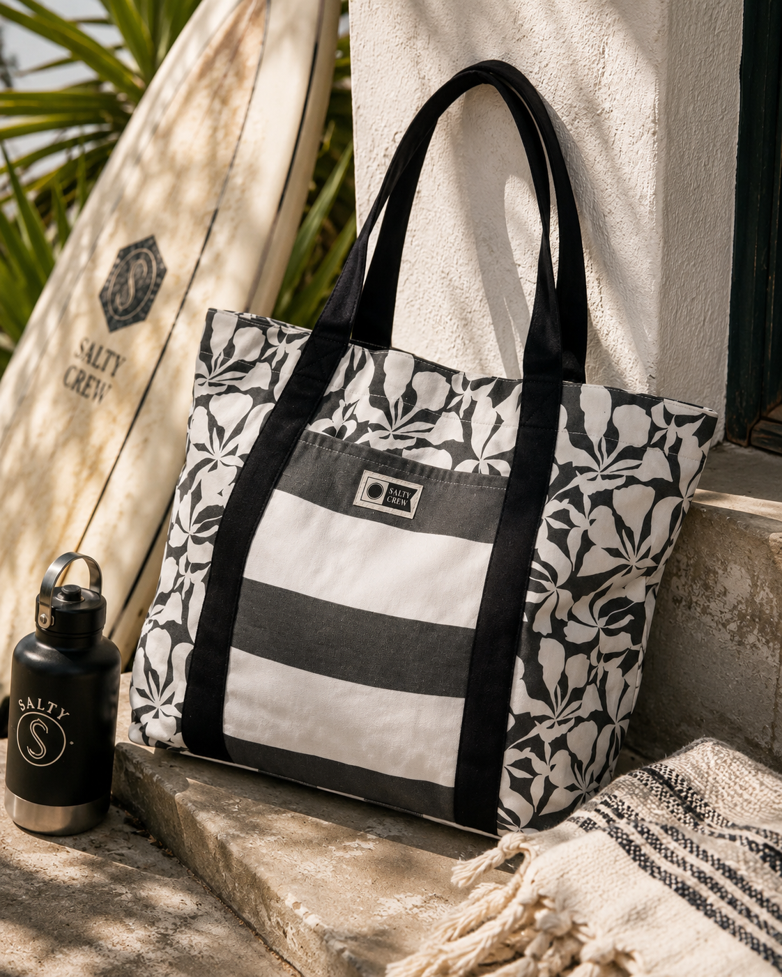 Bolso de playa Salty Crew Ashor Beach Bag Black para mujer en escena lifestyle surf junto a tabla de surf y accesorios premium de playa