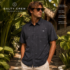 Camisa Salty Crew Micro Vibes SS Tech Woven Coal en jardín tropical de resort, fotografía editorial propia de THE SURF TOWN con modelo surf lifestyle, tejido técnico ligero y estilo premium para verano