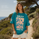 Camiseta Billabong Salty Since Deep Lagoon para mujer en fotografía editorial propia de THE SURF TOWN sobre sendero costero mediterráneo con luz natural de día y estilo surf lifestyle premium.