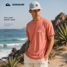 Camiseta Quiksilver Mini Logo Desert Sand en fotografía editorial propia de THE SURF TOWN junto a la costa, camiseta básica surf de hombre con logo frontal y estilo veraniego premium.