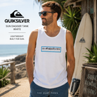 Camiseta Quiksilver Sun Dagger Tank White para hombre en entorno surf tropical, fotografía editorial propia de THE SURF TOWN, camiseta de tirantes blanca con logo frontal Quiksilver para verano, playa y surf lifestyle.