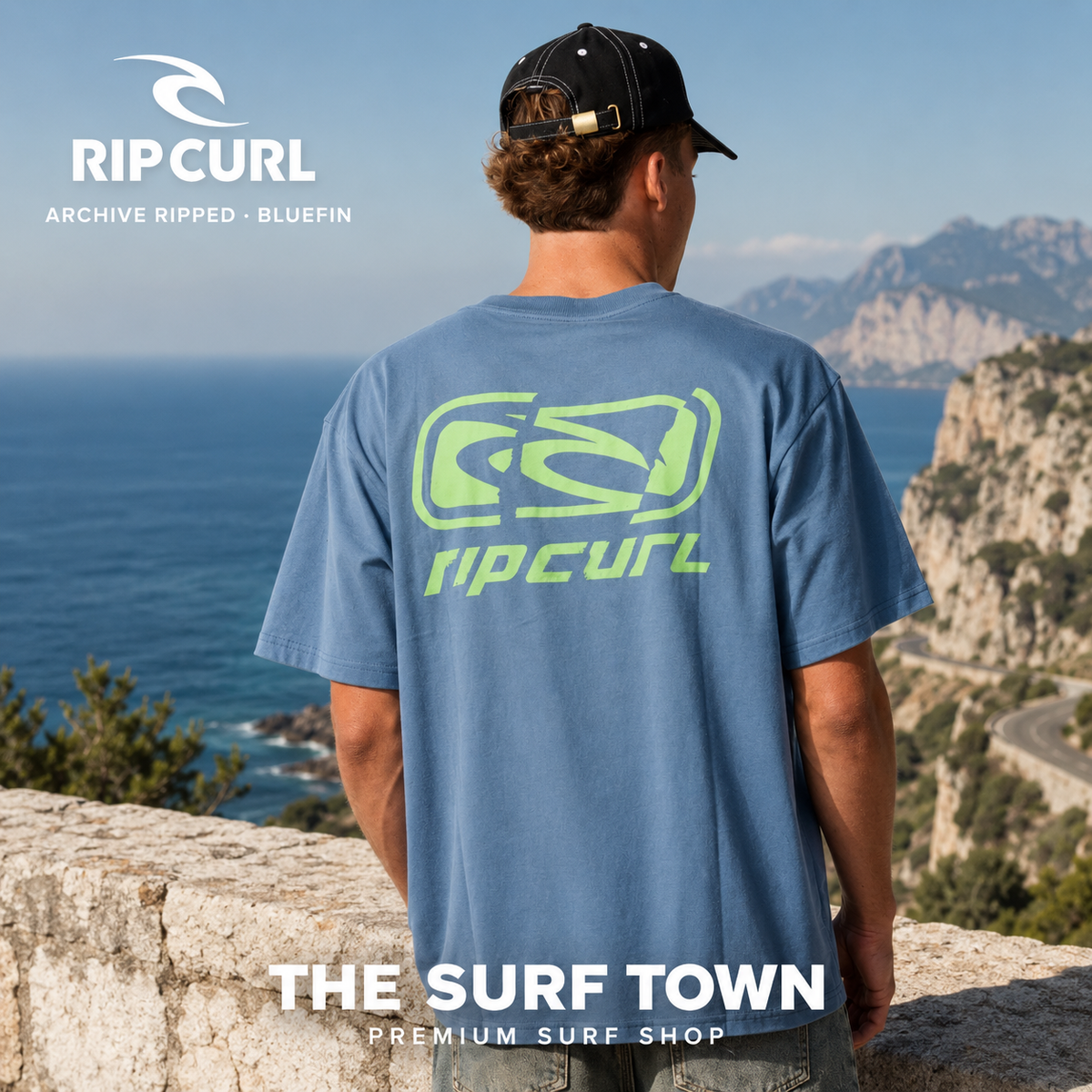 Camiseta Rip Curl Archive Ripped Loose Bluefin para hombre mostrando el gráfico trasero verde en un mirador costero, imagen editorial propia de THE SURF TOWN.