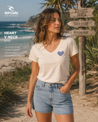 Camiseta Rip Curl Heart V Neck Bone mujer en escenario surf lifestyle premium con camiseta beige cuello pico y estética verano costera