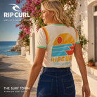 Camiseta de mujer Rip Curl Line Up Ringer Bone con ribetes verdes y gráfico retro multicolor, en una imagen editorial propia de THE SURF TOWN junto al Mediterráneo.