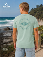 Camiseta Rip Curl Staple Tee Aloe Green hombre con estampado trasero surf en escenario lifestyle costero premium