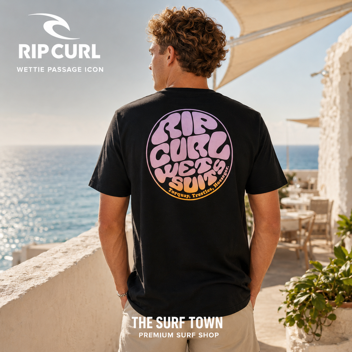 Camiseta Rip Curl Wettie Passage Icon Tee Black para hombre mostrando el gráfico trasero retro frente al mar, imagen editorial propia de THE SURF TOWN.
