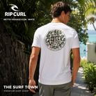 Camiseta Rip Curl Wettie Passage Icon Tee White para hombre mostrando el gráfico trasero retro en un jardín costero, imagen editorial propia de THE SURF TOWN.