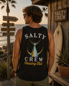 Camiseta sin mangas hombre Salty Crew negra en entorno surf shack premium al atardecer con cartel The Surf Town frente al mar Costa del Sol