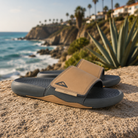 Chanclas pala Reef Cushion Phantom Slab Black Tan para hombre sobre piedra junto al mar con estilo surf lifestyle premium y ambiente Costa del Sol