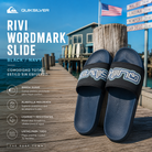 Chanclas de pala Quiksilver Rivi Wordmark Slide Black Navy sobre muelle de madera oceánico con estilo surf premium