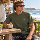 Camiseta Billabong Bad Dog Pill Wave - Verde (Rifle Green) en una escena lifestyle junto al mar; imagen editorial propia de THE SURF TOWN