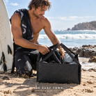 Cubo Cambiador Quiksilver Changing Surf Bucket - Negro (Black) en una escena lifestyle junto al mar; imagen editorial propia de THE SURF TOWN