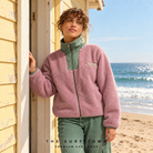 modelo llevando un forro polar billabong mountain life en la playa apoyada en una caseta en una imagen editorial propia de the surf town