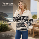 Forro polar Rip Curl Bossa Nova 1/4 Zip Black/White para mujer con estampado de palmeras, en una imagen editorial propia de THE SURF TOWN frente al océano.