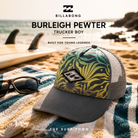 Gorra Billabong Burleigh Pewter Trucker Boy en fotografía editorial propia de THE SURF TOWN sobre toalla de playa junto al mar, estilo surf lifestyle de vacaciones para niño con diseño tropical y rejilla trasera.