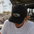 Gorra Billabong Origin Cap Black negra con bordado frontal en entorno surf lifestyle premium junto al mar