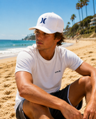 Gorra blanca Hurley hombre estilo surf premium en playa soleada junto al mar
