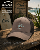 Gorra Oxbow Sandbar Driftwood Trucker marrón en escenario coastal premium con estética editorial surf cinematográfica