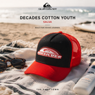 Gorra Quiksilver Decades Cotton Youth Salsa en fotografía editorial propia de THE SURF TOWN sobre toalla de playa junto al mar, estilo surf lifestyle de vacaciones y verano.
