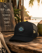 Gorra Rip Curl Custom Curve Black Purple estilo trucker en escenario surf lifestyle premium con estética coastal cinematográfica