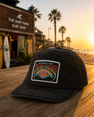 Gorra negra Rip Curl Padang Padang lifestyle surf premium sobre mesa de madera frente al mar al atardecer