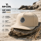 Gorra Rip Curl Surf Series Light Khaki en fotografía editorial propia de THE SURF TOWN con surfero esperando una ola en el pico, protección solar para nuca y cuello, diseño técnico surf UPF y estilo outdoor para largas sesiones en el agua.