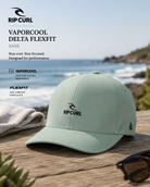 Gorra Rip Curl VaporCool Delta Flexfit Sage en escena surf lifestyle frente al mar con luz natural brillante