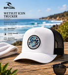 Gorra Rip Curl Wetsuit Icon Trucker Bone en escena surf lifestyle premium con luz natural brillante frente al mar