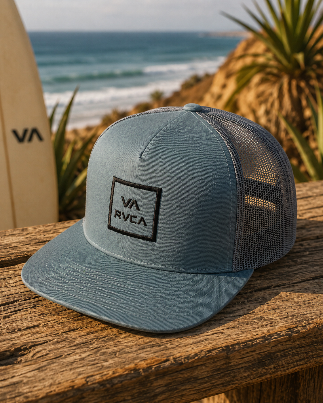 Gorra RVCA VA All The Way azul estilo surf lifestyle sobre mesa de madera junto al mar