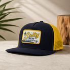 Gorra Salty Crew Ashore Trucker Navy Gold en entorno lifestyle premium con inspiración surf y estilo Costa del Sol