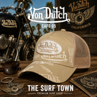 Gorra Von Dutch Cafe 05 en una fotografía editorial exclusiva creada por THE SURF TOWN con estética café racer, moto custom y luz natural diurna, destacando el estampado integral Von Dutch, el parche bordado premium y el diseño trucker en tonos beige.