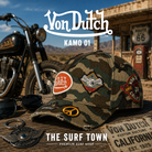 Gorra Von Dutch Kamo 01 en una fotografía editorial exclusiva creada por THE SURF TOWN con estética café racer, Route 66 y luz natural diurna, destacando el estampado camuflaje clásico, los parches bordados y el diseño premium.