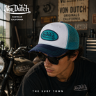 Gorra Von Dutch Sum Blue blanca, azul marino y turquesa con rejilla trasera en fotografía editorial propia de THE SURF TOWN ambientada en un taller custom vintage inspirado en la cultura motera californiana y el estilo trucker americano.