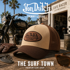 Gorra Von Dutch Terry Log01 en una fotografía editorial exclusiva creada por THE SURF TOWN con estética café racer, moto custom y luz natural diurna, destacando el parche bordado Von Dutch, el diseño trucker premium y los tonos beige y marrón.
