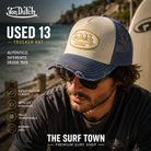 Gorra Von Dutch Used 13 trucker beige y azul con parche California y visera desgastada en escena lifestyle costera de THE SURF TOWN