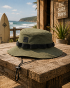 Gorro Billabong bucket hat militar hombre estilo surf lifestyle sobre mesa de madera frente al mar