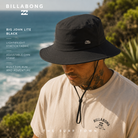 Gorro Billabong Big John Lite Black en fotografía editorial propia de THE SURF TOWN sobre acantilados junto al mar, diseño técnico con cordón ajustable y protección solar para surf, playa y outdoor.