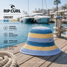 Gorro Rip Curl Crochet Blue Natural en fotografía editorial propia de THE SURF TOWN en marina mediterránea premium con diseño crochet, estilo surf veraniego, protección solar y acabado artesanal para playa y vacaciones.
