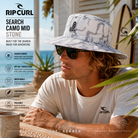Gorro Rip Curl Search Camo Mid Stone en fotografía editorial propia de THE SURF TOWN en beach house australiana frente al mar con diseño camo, protección solar, estilo surf adventure y uso outdoor para playa, viajes y exploración.