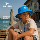 Gorro Rip Curl Shred Blue Kids azul para niños con protección solar en muelle surf junto al mar