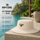 Gorro Rip Curl UPF Premium Surf Bone Black en fotografía editorial propia de THE SURF TOWN junto a piscina infinity tropical con protección solar UPF 50+, diseño surf premium y estilo outdoor para playa, viajes y actividades al aire libre.