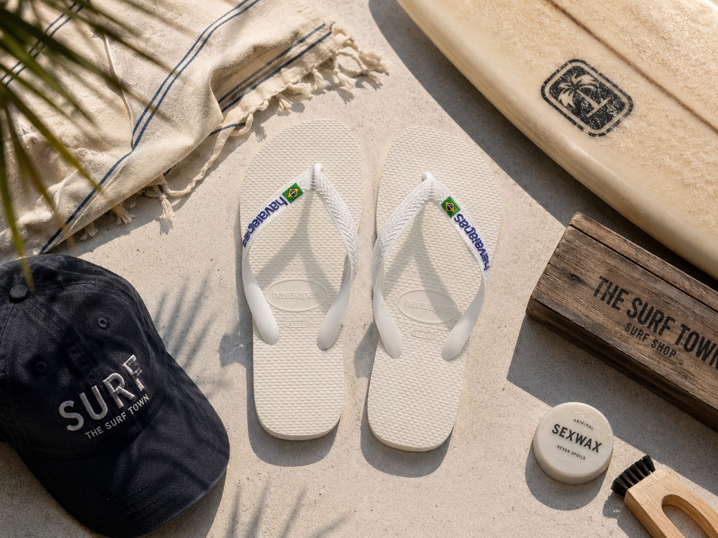 Chanclas Havaianas Brasil Logo blancas sobre suelo mediterráneo junto a tabla de surf y accesorios beach lifestyle premium con detalle The Surf Town Surf Shop