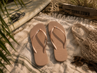 Chanclas Havaianas Slim Crystal Rose Gold para mujer sobre manta beige junto a tabla de surf en ambiente beach lifestyle premium con detalle The Surf Town