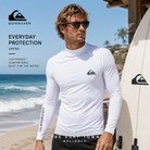 Licra Quiksilver Everyday UPF50 LS White en fotografía editorial propia de THE SURF TOWN junto al mar con tabla de surf y estilo surf performance premium bajo luz natural diurna