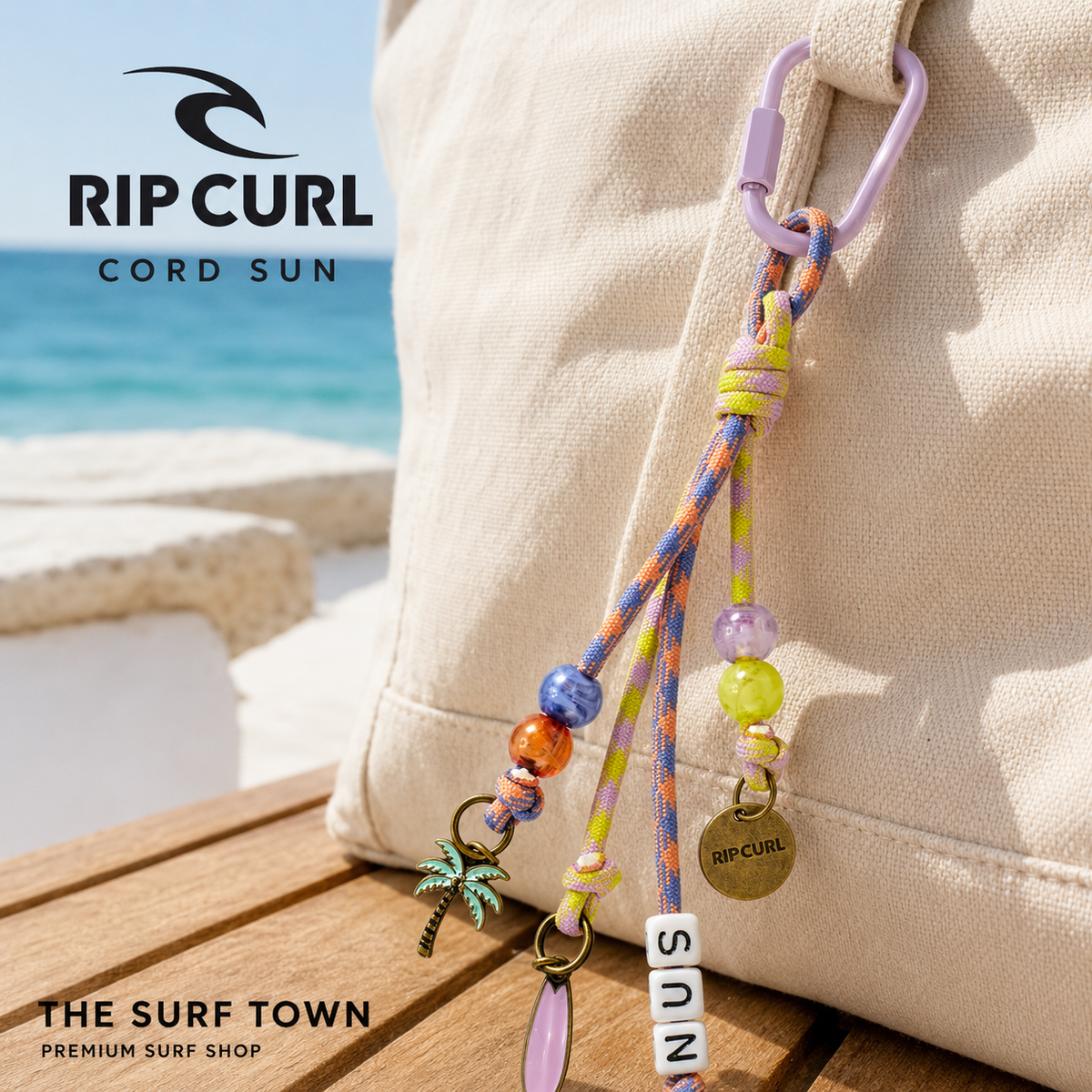 Llavero Rip Curl Cord Sun multicolor con cordones, abalorios y colgantes costeros, sujeto a un bolso en una imagen editorial propia de THE SURF TOWN.