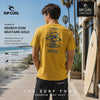 modelo vistiendo una Camiseta Rip Curl Search Icon Mustard Gold durante un video propio promocional de the surf town junto a una tienda de surf rip curl